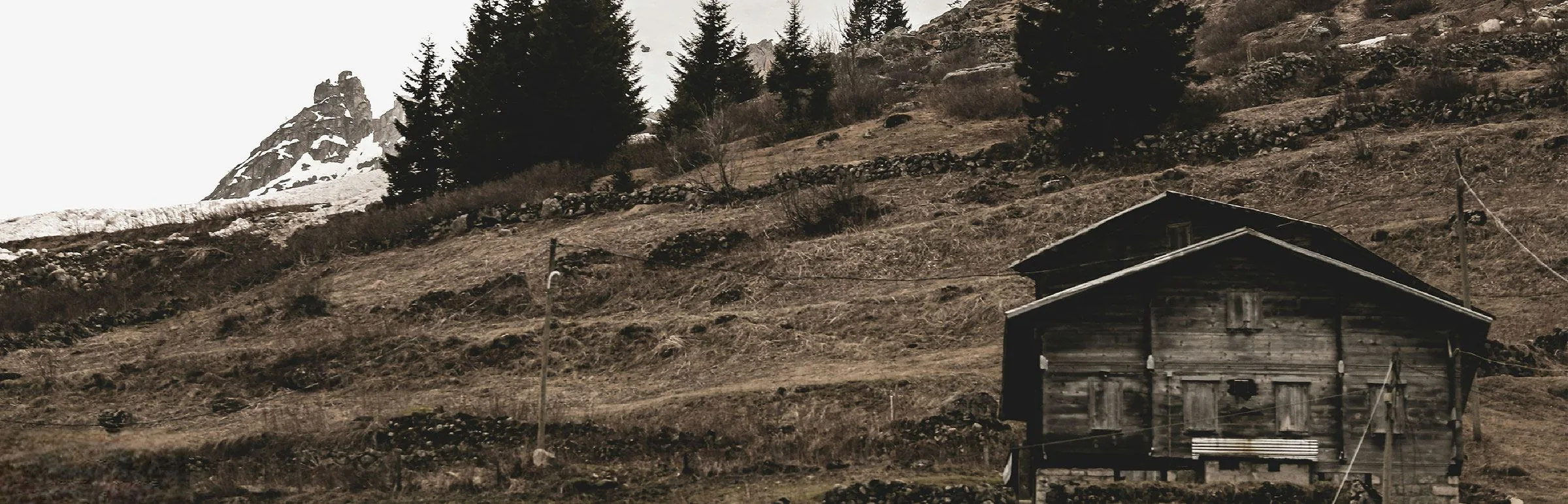 Cabane en bois isolée sur un alpage, sommet enneigé en arrière-plan