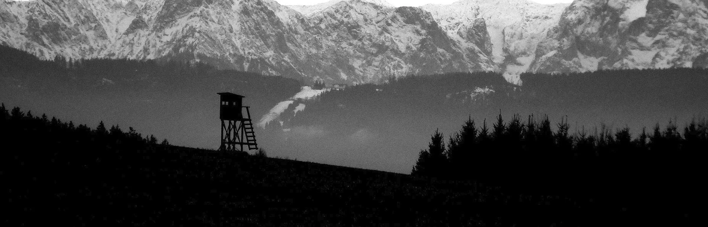 Mirador de chasse à l'affût face aux montagnes enneigées, en noir et blanc