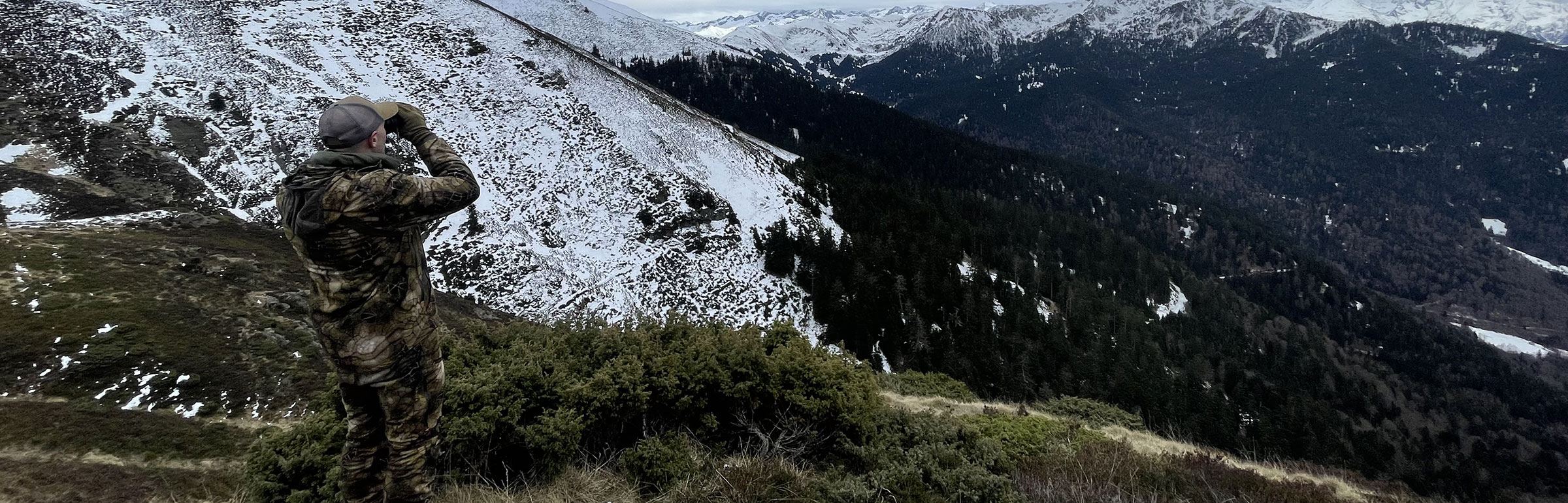 Chasseur observant aux jumelles un vallon de montagne enneigé